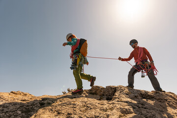 Two people are climbing a mountain together. One of them is wearing a red shirt. The other person is wearing a yellow shirt