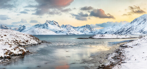 Stunning morning view of Torsfjorden fjord with cracked ice and snowy mountain peaks at background.