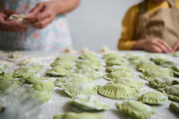 Selective focus on sculpted homemade dumplings on floured table against the background of young mom and daughter cooking together