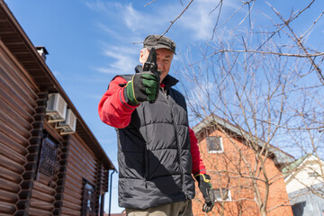 gardening scissors for trimming thin tree branches in the hand of a man wearing gardening gloves, who is standing in the garden next to the house against the blue sky. High quality photo