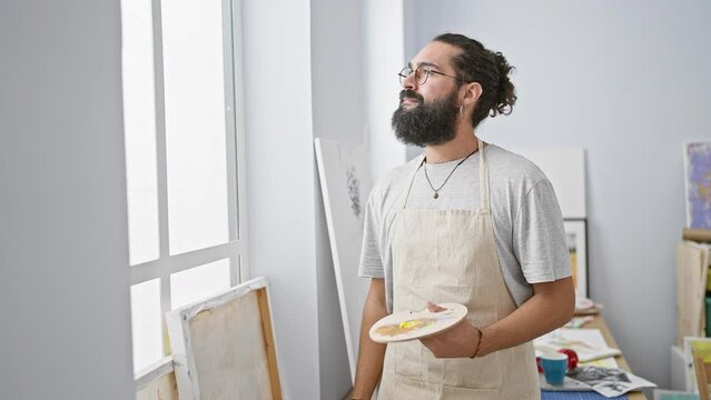 Hispanic man with beard and apron holding a paint palette in an art studio