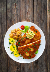 Crispy breaded fried pork loin chops with fries and fresh vegetables on wooden table
 - obrazy, fototapety, plakaty