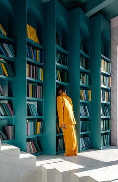 Anonymous female in formal suit leaning on bookshelf 