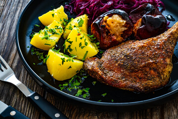 Roast duck thigh with boiled potatoes, apples and red cabbage on wooden table

