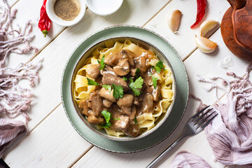 Dinner dish: pasta with mushrooms, cream sauce and meat in a plate on a white background.