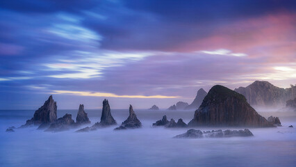 warm sunrise on the beach of Gueirua, Asturias with a dramatic sky and the high tide partially...