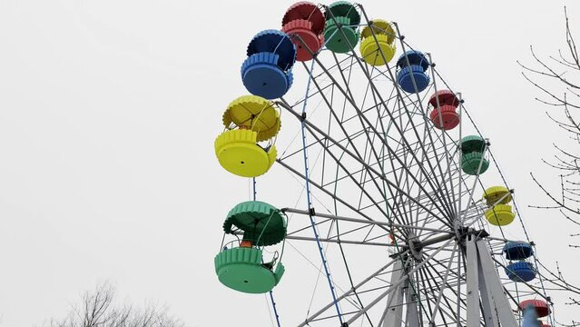 The old Ferris wheel rotates without visitors in the amusement park in cloudy weather