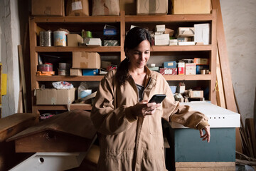 Relaxed female worker using phone at small workshop 