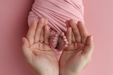 The palms of the father, the mother are holding the foot of the newborn baby in a pink blanket....