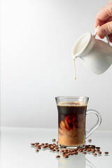 A man's hand pours cream into a glass of coffee. - obrazy, fototapety, plakaty
