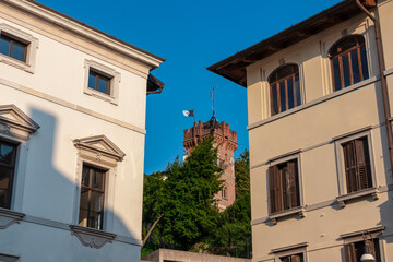 Stroll along narrow urban street that meanders towards magnificent ancient city center of charming town of Udine, Friuli Venezia Giulia, Italy, Europe. Looking at tower of castle through houses