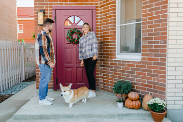 Couple with a dog standing near the door with a christmas wreath 