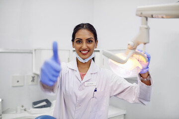 Dentist, portrait and thumbs up in office with smile for support, care and good dental health. Woman, equipment and happy with hand gesture for motivation, approval and success in oral hygiene
