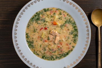 Fresh creamy salmon fish soup with potatoes, carrots, broccoli, peppers and onions in a ceramic plate on a wooden table. A delicious dinner consists of fish soup with salmon