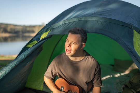 A young man with Down syndrome camping is playing the ukulele