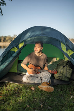 A young man with Down syndrome camping is playing the ukulele