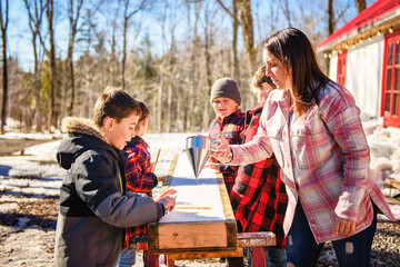 Photo showing children tasting maple syrup with wooden spoon - 777682622