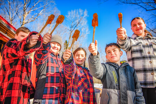 Photo showing children tasting maple syrup with wooden spoon