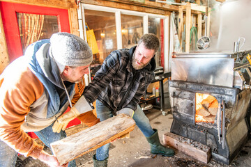 sugar shack, two maple farmers wearing a traditional clothe working doing sugar sirop and puting some wood on fire - 777684491