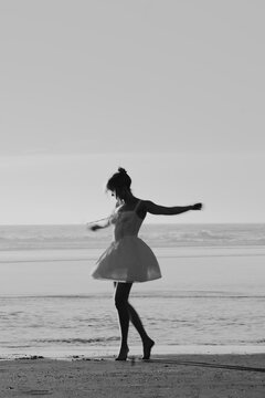 Black and White image of a woman dancing in a white dress by the sea