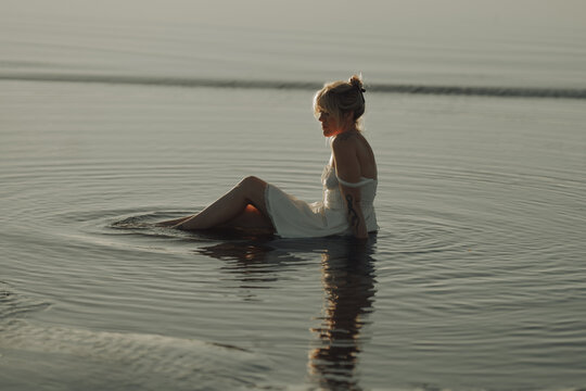 Woman sitting in the water in a white dress