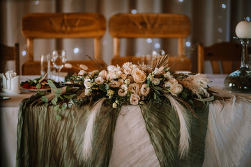 Close-up of a wedding table's floral arrangement and table setting featuring roses, greenery,...