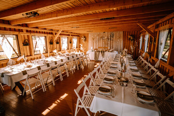 Valmiera, Latvia - Augist 13, 2023 - A rustic wedding reception setup inside a wooden lodge with long tables, white chairs, elegant table settings, and twinkling lights.