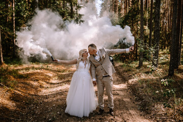 Valmiera, Latvia - Augist 13, 2023 - A bride and groom joyfully hold smoke bombs in a forest,...