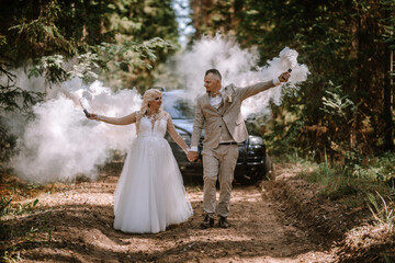 Valmiera, Latvia - Augist 13, 2023 - A bride and groom hold hands and set off smoke bombs on a...