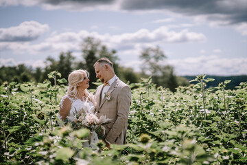 Valmiera, Latvia - Augist 13, 2023 - A bride and groom are nestled among green plants, sharing a...
