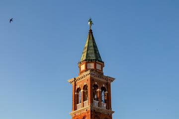 Close up view at sunrise of bell tower of Church of Saint James Apostle in charming town of Chioggia, Venetian Lagoon, Veneto, Italy. Sightseeing in historic old town. First sun beams on landmark