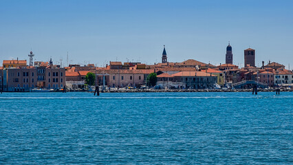 Fototapeta na wymiar Panoramic view of historic landmarks of charming town of Chioggia seen from Sottomarina, Venetian Lagoon, Italy. Seagull sitting on wooden pole. Known as little Venice. Urban vacation in summer