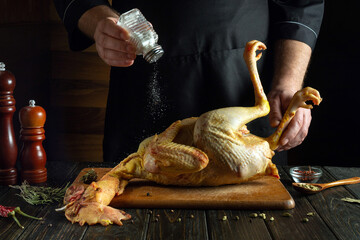 A cook prepares a raw rooster on the kitchen table in a restaurant. Before roasting, the chef adds...