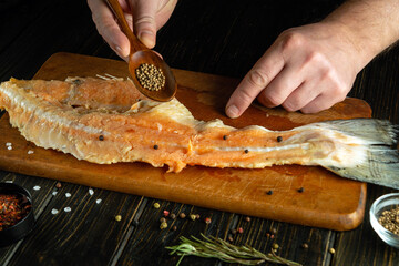 The cook is preparing a steak from raw fish on the kitchen table. Add aromatic coriander to the...