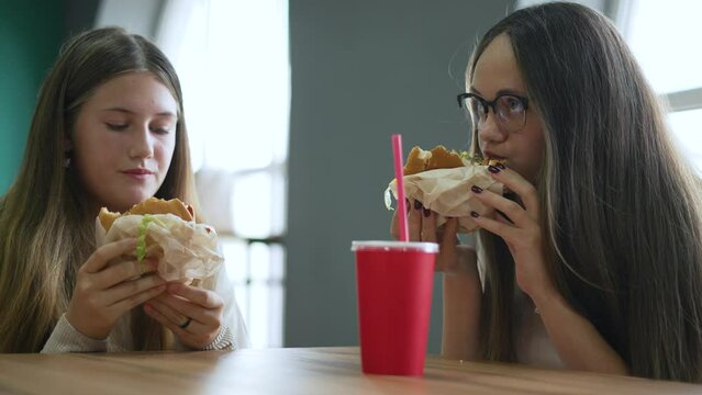 Portrait of girls by window in fast food restaurant.group of people spend weekend in fast food restaurant with burger.girls enjoying delicious burger.girls eating burger against background of window