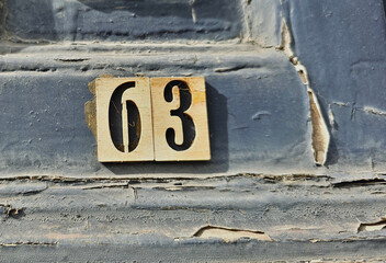 House number sixty three or 63 made of wood. On a wooden surface covered with old blue paint