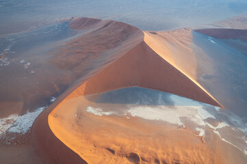 Breathtaking sunrise over the sand dunes of Sossusvlei, Namibia, captured from a helicopter. The first light of dawn casts dramatic shadows and highlights the vibrant colors of the desert. © Felix