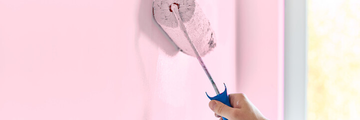 Male hand painting wall with paint roller. Painting apartment, renovating with light pink color...