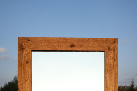 Wooden frame mirror reflecting clear sky surrounded by nature outdoors