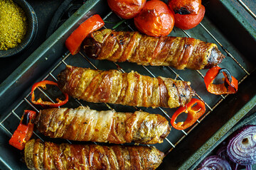 Grilled bacon wrapped sausages with tomatoes and onions on baking tray top view, close-up - 777701232