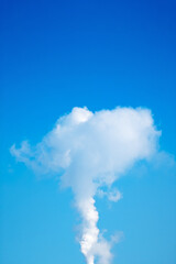 Cloud of smoke is rising into the sky above a clear blue sky. The smoke is white and billowing, creating a sense of movement and energy. The contrast between the smoke