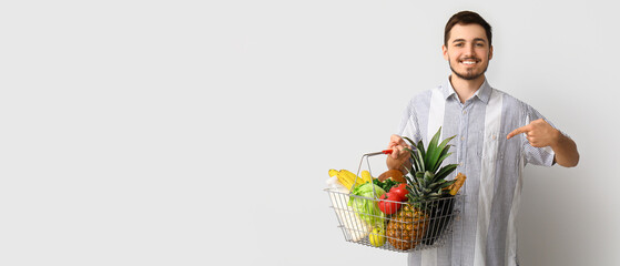 Young man pointing at shopping basket on white background