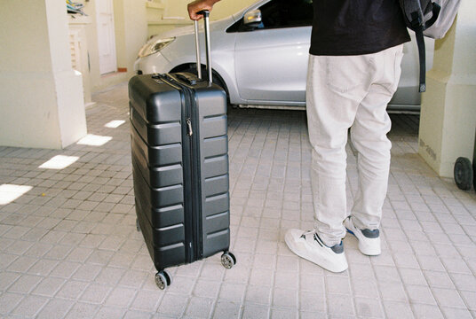 A man with a travel suitcase by the car