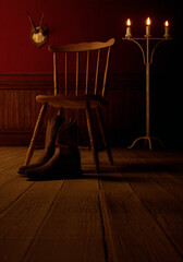 Vintage rustic interior with leather cowboy boots, wooden floor, wooden chair, paneling, candlestick and deer skull on the wall.