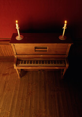 Vintage rustic interior with vintage piano with candles on it on wooden floor against red wallpaper with wooden paneling.