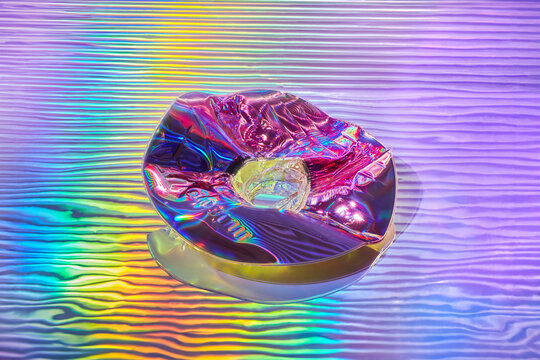 Wavy water surface with cracked compact disc and holographic light