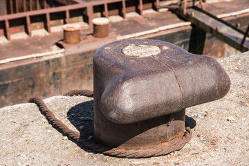 Old metal dock mooring pole with steel rope for securing river bulk barge ship closeup