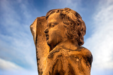 Baroque sculpture in brown stone of a cherub with curly hair located in a Spanish cloister with an intense blue background with clouds