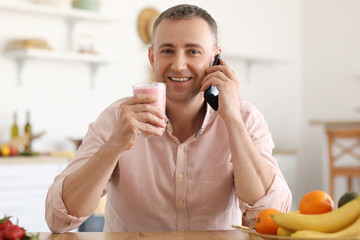Mature man with glass of fresh fruit smoothie talking by mobile phone in kitchen