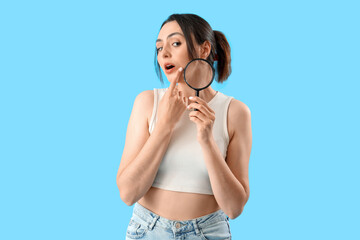 Young woman with magnifier on blue background